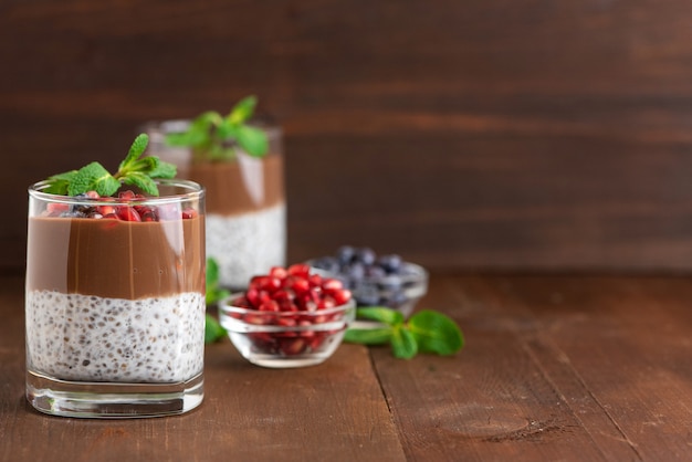 Dark brown chocolate chia seed pudding in a glass topped with a spoonful of creamy peanut butter and grated chocolate.