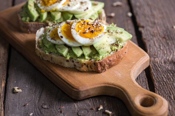 A fresh slice of avocado toast topped with a halved hard-boiled egg and sesame seeds on a desk.
