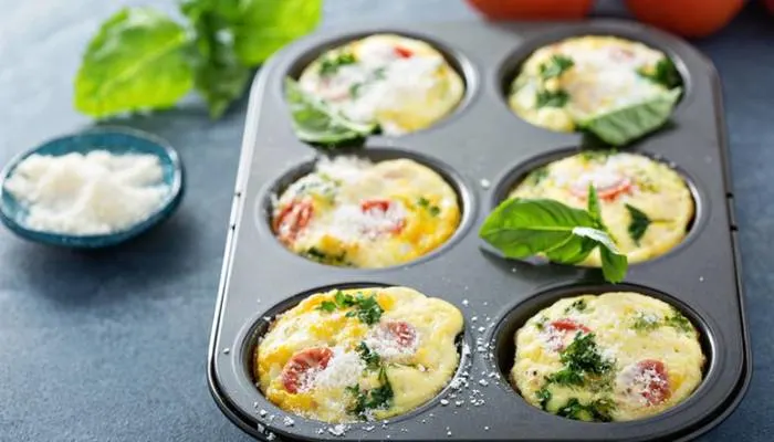 A batch of freshly baked mini egg frittatas with vegetables in a muffin tin on a kitchen counter.